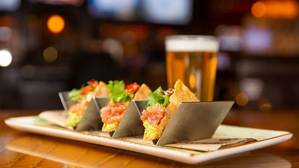 Four crispy gourmet tacos with protein and greens on a table.