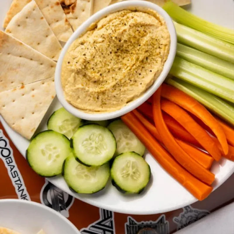 Overhead close-up of hummus platter with pita, celery, carrots, cucumber.