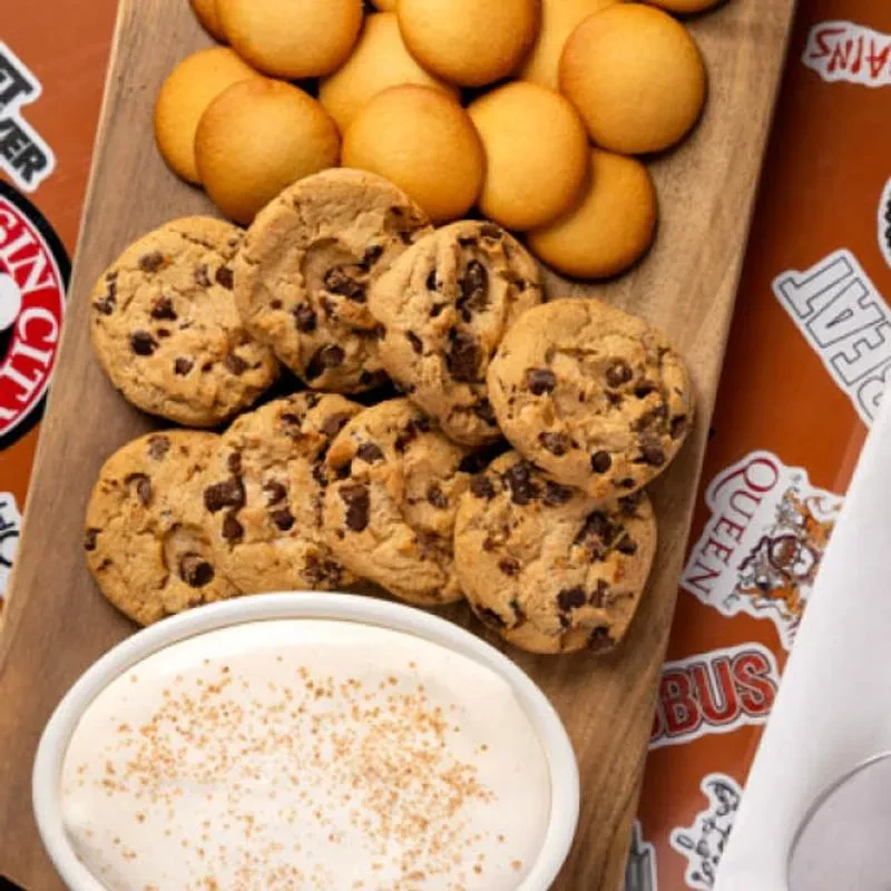 Assorted vanilla wafers, chocolate chip cookies, and creamy dip on a cutting board.