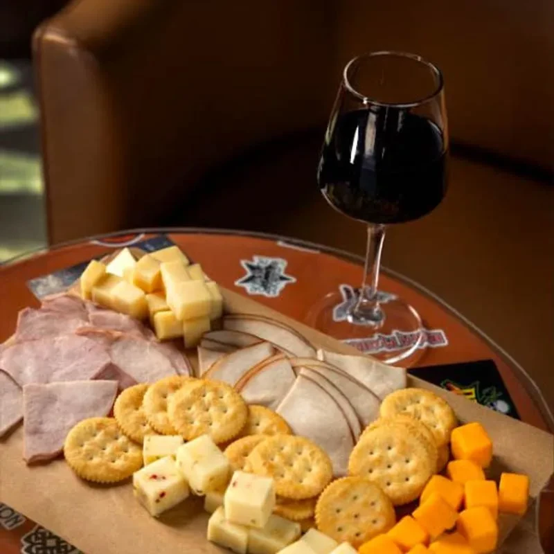 Rustic charcuterie board with meats, cheeses, crackers, red wine glass.