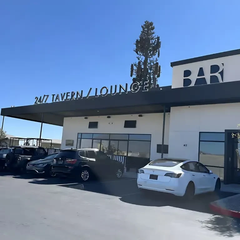 Modern white building with '24/7 TAVERN LOUNGE' sign and parked cars.
