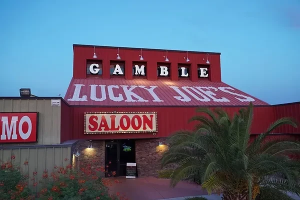 Vibrant red Lucky Joes Saloon building with illuminated signs and palm trees.