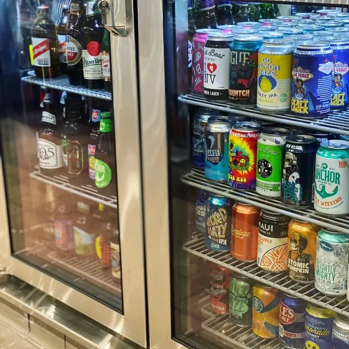 Double-door commercial cooler filled with beer bottles and colorful craft cans.