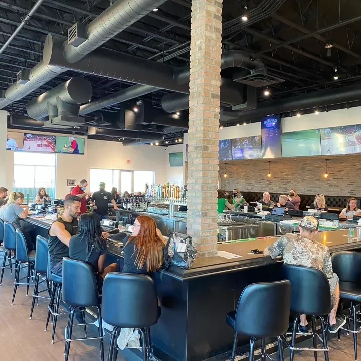 Bustling, modern sports bar interior with patrons, TVs, and industrial decor.