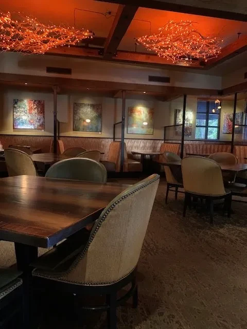 Restaurant interior with wooden beams, glowing branch chandeliers, and cozy seating.
