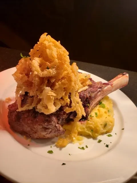 Reddish-brown steak topped with fried onions and mashed potatoes on a white plate.