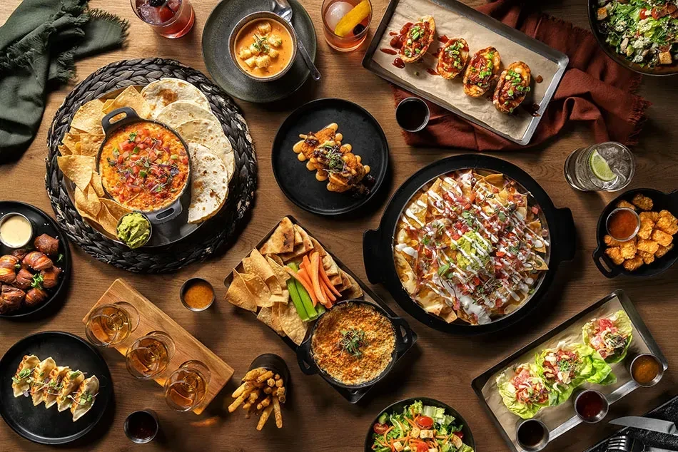 Overhead flat-lay of numerous appetizers, shared dishes, and drinks.