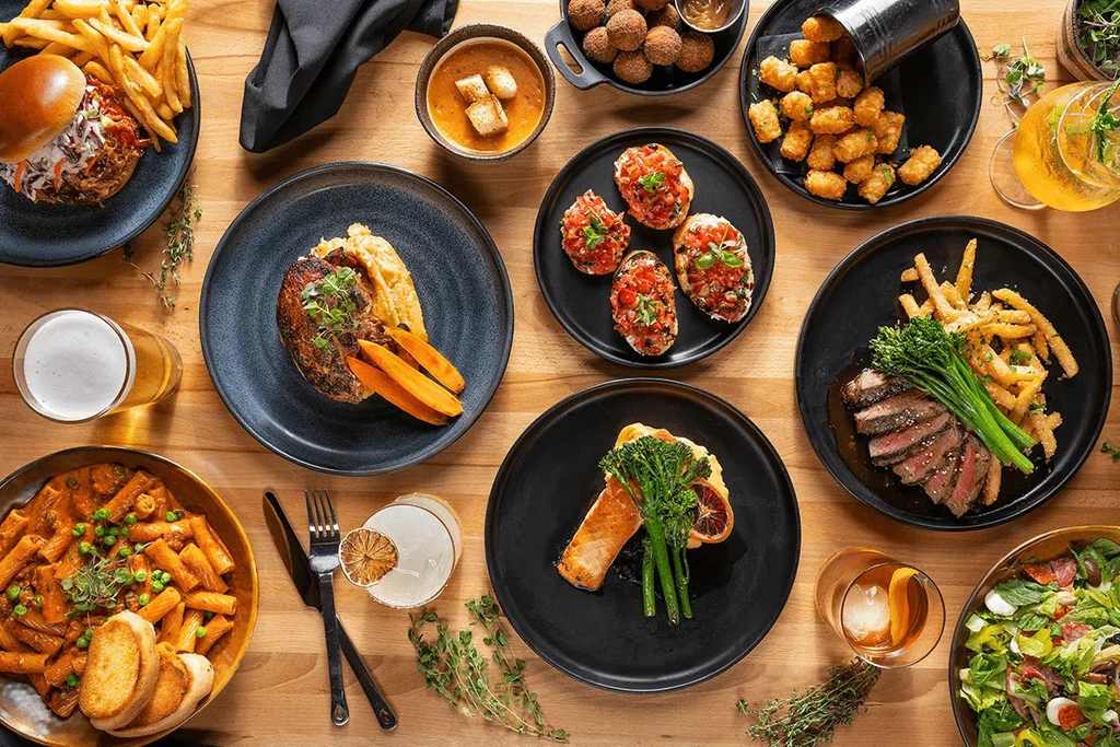 Flat lay of diverse food and drinks on a light wooden table.