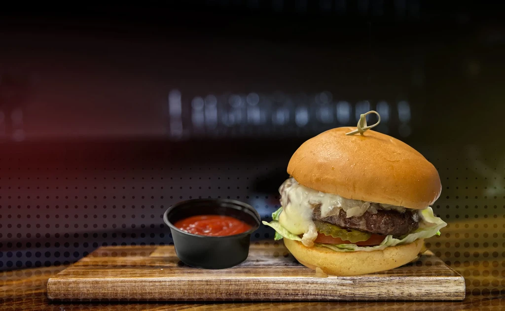 Gourmet burger with cheese, caramelized onions, red sauce on wood.