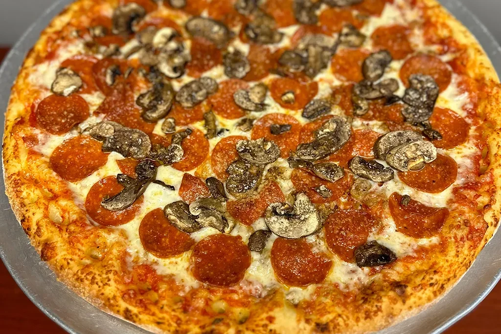 Golden-brown pizza with mozzarella, pepperoni, and mushrooms on a metal pan.