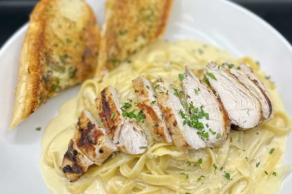 Creamy pasta with grilled chicken, herbs, and garlic bread.