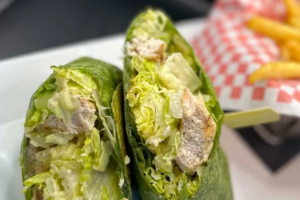 Halved green wrap showing chicken, lettuce, dressing, with fries in background.