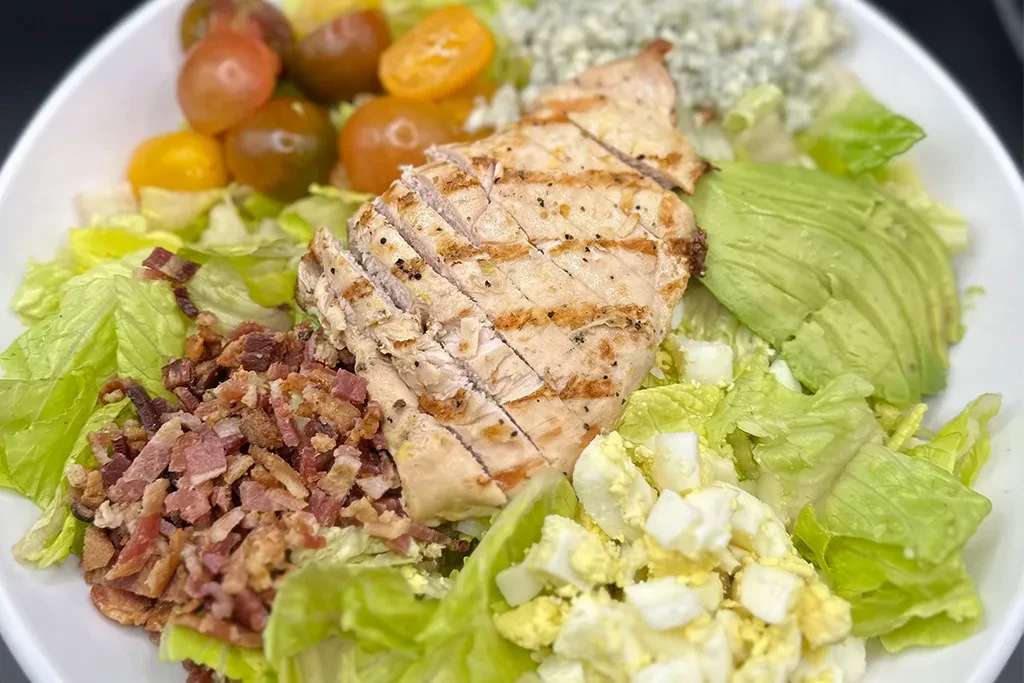 Close-up of a Cobb salad with grilled chicken, avocado, bacon, egg, tomatoes.