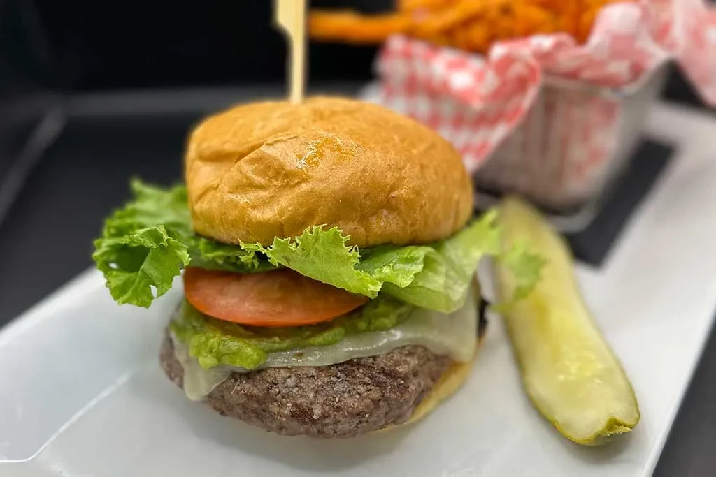 Gourmet burger with cheese, guacamole, pickle, and sweet potato fries.