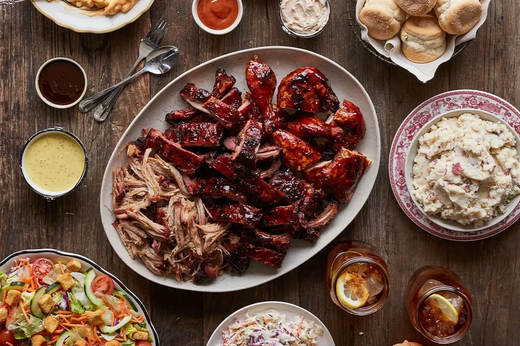 Vibrant overhead view of barbecued meats, sides, and drinks on wooden table.
