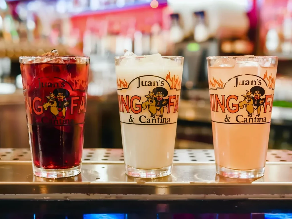 Three branded glasses with red, white, and pink drinks on a bar.