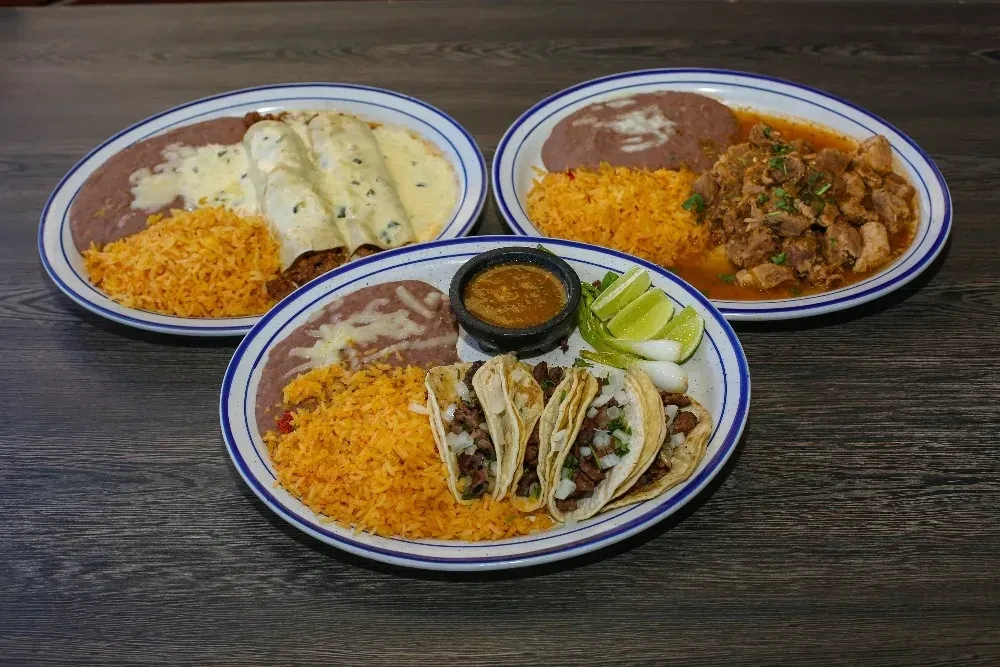Three plates of Mexican enchiladas, stew, and tacos on a table.