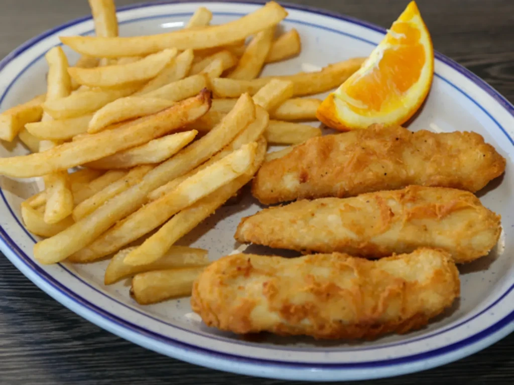 Golden-brown battered fish, french fries, and orange wedge on striped plate.