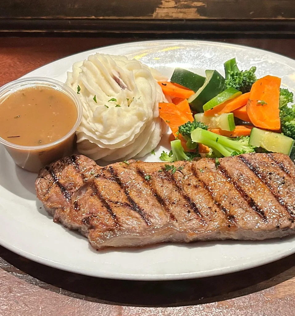 Grilled steak, mashed potatoes, steamed vegetables, and gravy on a plate.
