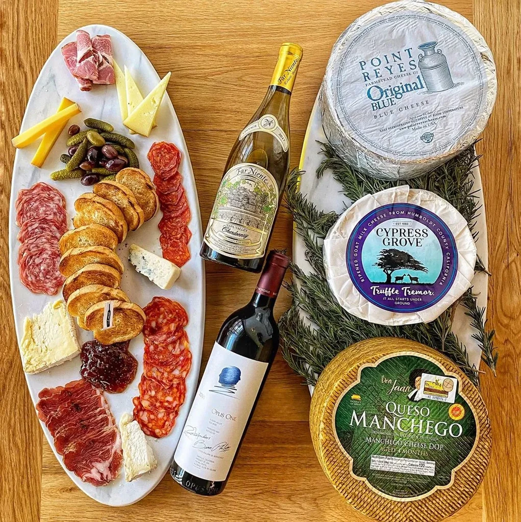 Charcuterie and cheese board with two wine bottles and whole cheese wheels.