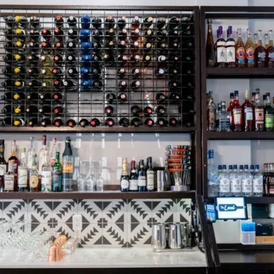 Organized, modern bar with extensive wine and liquor selection, geometric tiles.