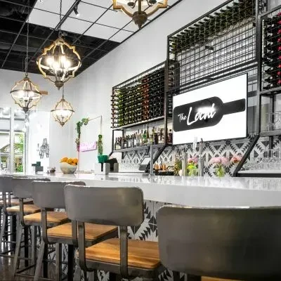 Modern bar area with white counter, wine racks, and "The Local" screen.