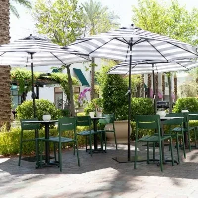 Outdoor cafe with tables, chairs, and striped umbrellas surrounded by lush foliage.