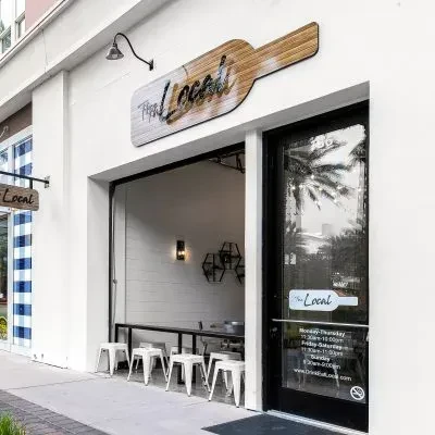 The Local restaurant exterior with open entrance, wine bottle sign, palm reflection.
