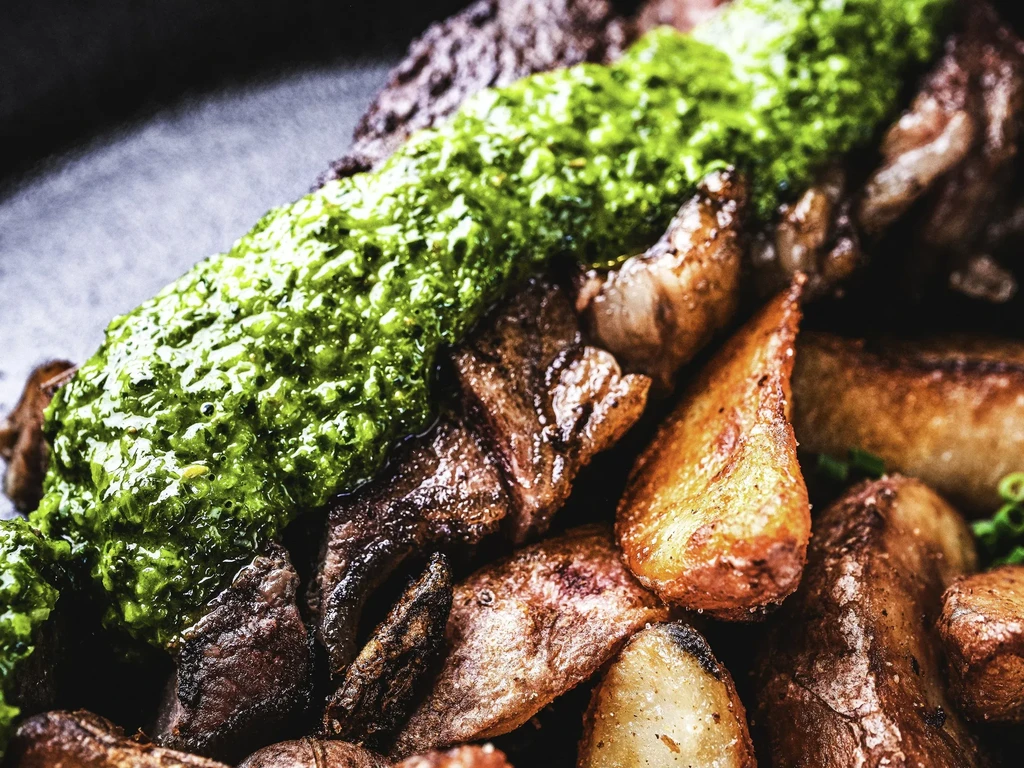 Seared steak with vibrant green sauce and golden crispy potatoes.