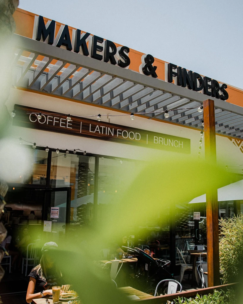 MAKERS & FINDERS restaurant exterior, outdoor dining, blurred foreground foliage.