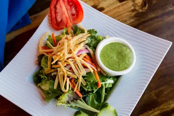 Fresh salad with lettuce, carrots, onions, crispy tortilla strips, and green dressing.