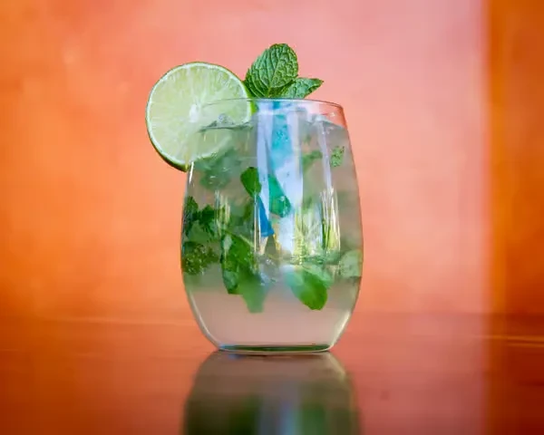 Lime and mint cocktail in clear glass with ice and garnishes.