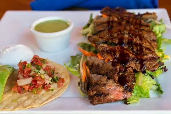 Grilled meat, lettuce, pico de gallo, tortilla, and sauces on a plate.
