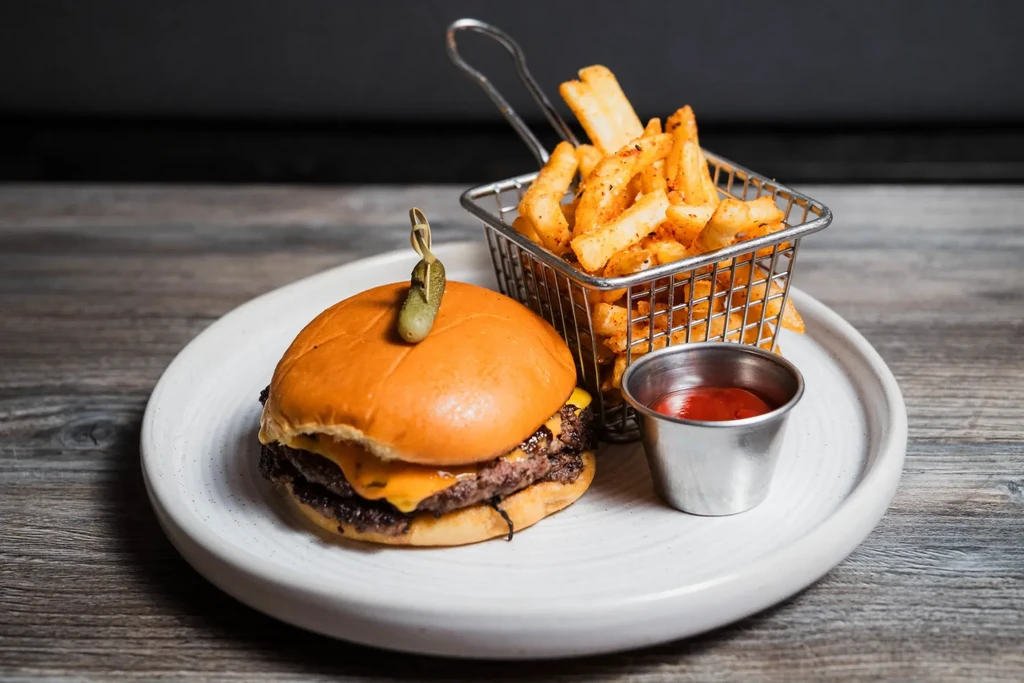 A double cheeseburger, fries, and ketchup on a rustic wooden table.