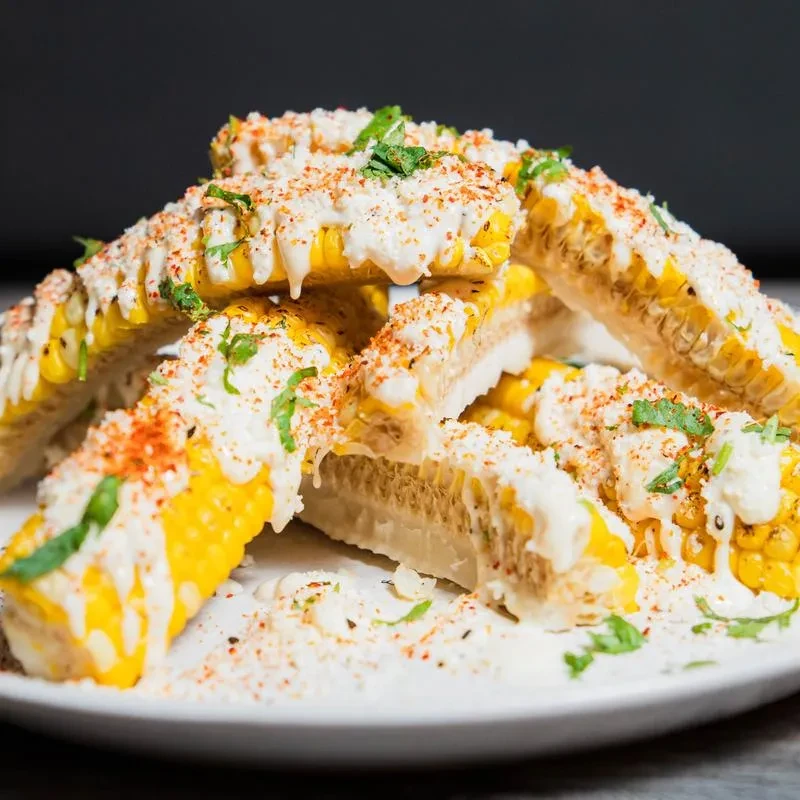 Cut corn on the cob with creamy sauce, red seasoning, and green herbs.