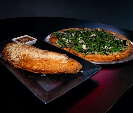 Calzone with cheese and sauce, next to an arugula pizza.