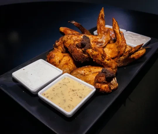 Platter of crispy, golden-brown chicken wings with two dipping sauces.