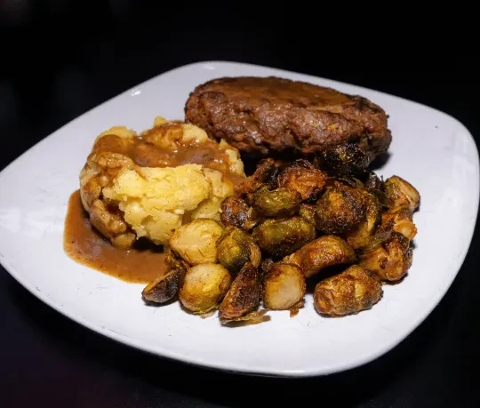 Salisbury steak with mashed potatoes, gravy, and roasted Brussels sprouts.