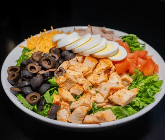 A generous salad with chicken, eggs, tomatoes, olives, and shredded cheese.