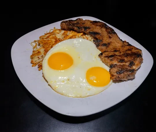 Two sunny-side-up eggs, hash browns, and grilled meat on a white plate.