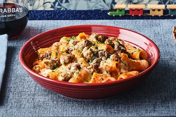 Close-up of tubular pasta with meat sauce, wine, and wooden train cars.