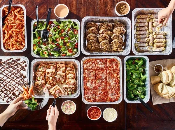 Flat-lay of a catering spread with pasta, pizza, salads, and desserts.