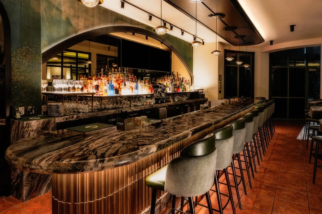 Upscale bar with dark marble counter, illuminated bottles, and green wall.