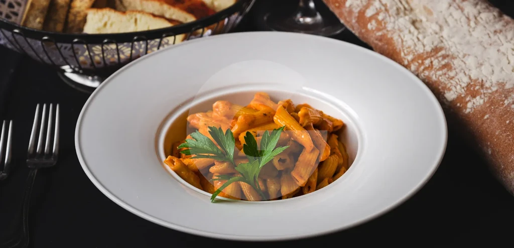 Top-down: Penne pasta with red sauce, parsley, bread, and fork.