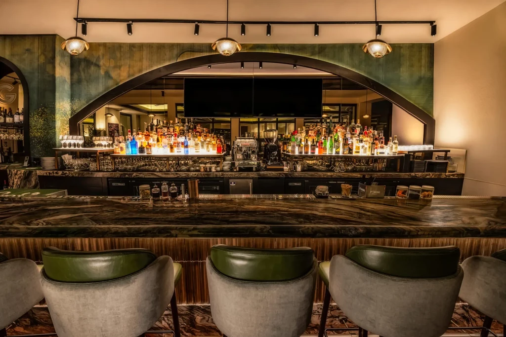 Sophisticated bar with illuminated liquor display, marble counter, and stools.