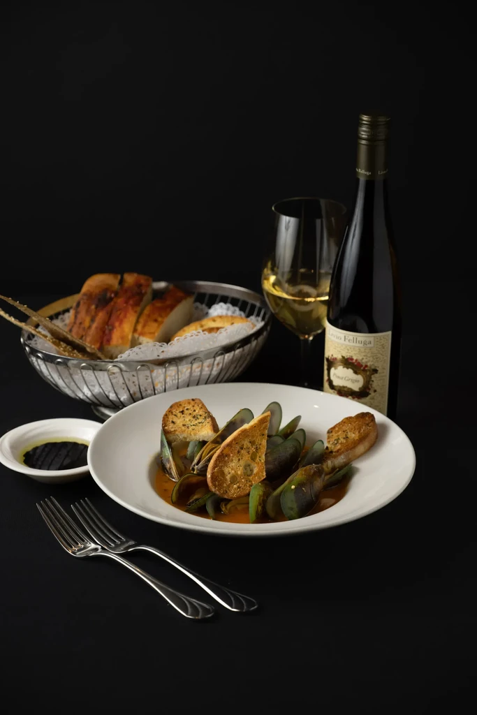 Green-shelled mussels with toasted bread, white wine, and silver forks.