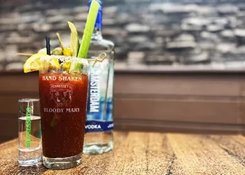 Elaborately garnished Bloody Mary cocktail with branded glass and chaser.