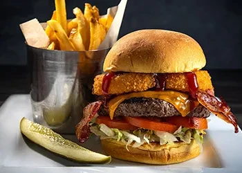 Deluxe burger with melted cheese, bacon, fries, and a pickle.