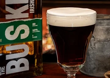Dark stout beer in fluted glass beside a Bushmills Irish Whiskey bottle.