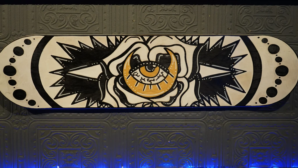 Custom skateboard deck, black, white, gold eye-moon design, on grey wall.